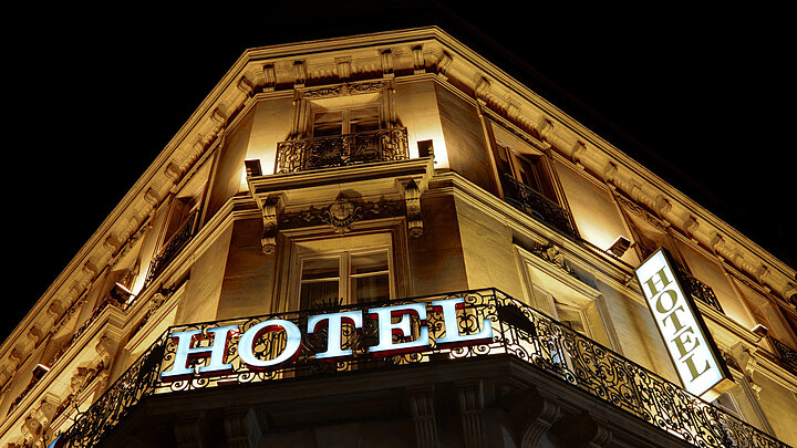 Zdjęcie dekoracyjne oświetlonej ściany budynku z świecącym napisem HOTEL. Zdjęcie zrobione nocą, w tle czarne niebo.